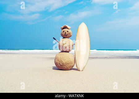 Bonhomme de sable dans le sable sur la plage avec une planche de surf sur l'arrière-plan de la belle mer et ciel bleu. concept de surf et divertissements en mer Banque D'Images