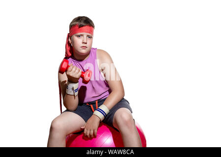 L'enfant est assis sur un fitball rose dans un survêtement et avec un bandage sur sa tête et les trains biceps Banque D'Images
