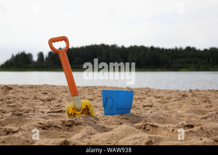 Godet pelle et bébé dans le sable sur la rive du fleuve et fond en bois Banque D'Images
