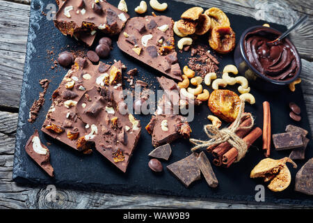 Barre de chocolat au lait sucré fait maison avec les figues séchées et remplissage de cajou sur pièces sur un plateau en ardoise noire avec des ingrédients, vue horizontale à partir de ci-dessus, Banque D'Images