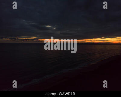 Coucher du soleil et se détendre vol au dessus de l'océan avec un ciel dramatique et la nuit à venir au pêcheur seul qui de loin ressemble à un petit isolement Banque D'Images