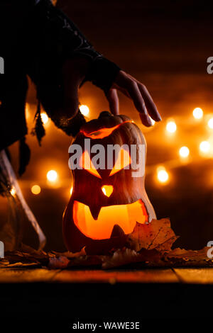 Photo de halloween citrouille coupées en forme de visage avec la main de la sorcière sur l'arrière-plan avec la combustion de feux jaunes Banque D'Images
