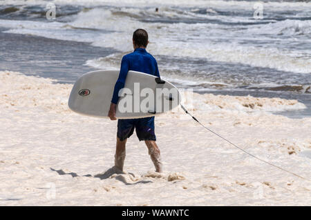 Un internaute se promener le long de l'écume d'une plage dans la mousse brune qui se sont produits le long des plages à la tête d'Alexandra sur la Sunshine Coast dans le Queensland, Australie Banque D'Images