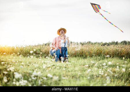 Père fils colorés avec le lancement d'air cerf-volant sur le terrain pendant le coucher du soleil. Concept d'une famille heureuse s'amusant pendant l'activité estivale Banque D'Images