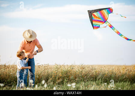 Père fils colorés avec le lancement d'air cerf-volant sur le terrain pendant le coucher du soleil. Concept d'une famille heureuse s'amusant pendant l'activité estivale Banque D'Images