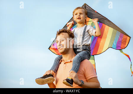 Portrait d'un heureux père et fils sur les épaules avec l'air sur le cerf-volant coloré fond de ciel bleu. Concept d'une famille heureuse et d'acti Banque D'Images