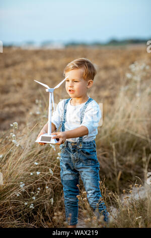 Jeune garçon curieux Playing with toy wind turbine sur le terrain, étudier comment fonctionne l'énergie verte d'un jeune âge Banque D'Images