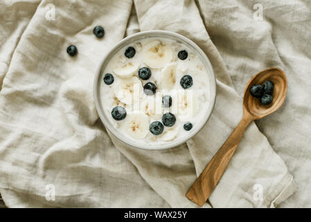 Petit-déjeuner sain avec du yogourt et granola avoine, bananes et les bleuets dans un bol. Fond gris, vue du dessus. délicieux gruau aux fruits rouges. vegan foo Banque D'Images