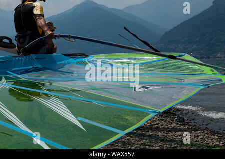 Le lac de Côme, Italie - 21 juillet 2019. Windsurfer homme portant un voile dans le lac de montagne, surf board close-up. Alp mountains sur un arrière-plan. Banque D'Images