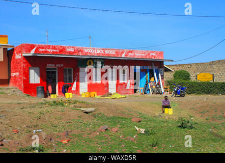 Petites boutiques sur le côté de la route, Kenya, Afrique. Les gens de la région à l'extérieur vendant des conteneurs d'eau. Boutique nommée « Good Luck House » Banque D'Images