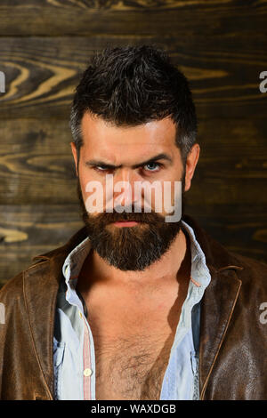 Hipster grave dans un barbier, look. Hipster avec barbe, visage sérieux sur fond de bois. Banque D'Images