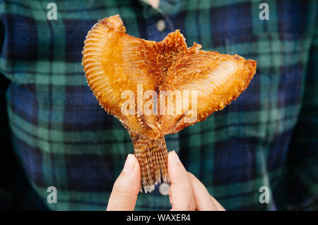 Petit morceau de croustillant de poisson Tilapia frit d'or dans la main femme Banque D'Images