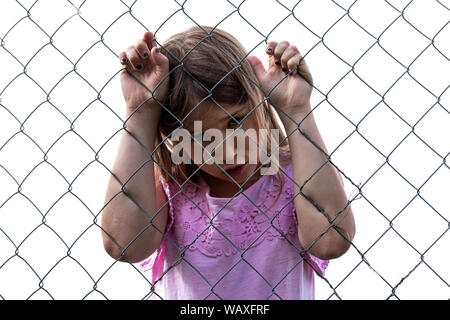 Sad girl derrière metal wire mesh fence. Enfant solitaire et abandonnée à l'extérieur. Déprimé preteen aux yeux clos tenant la cage d'acier chaîne. Loneline Banque D'Images