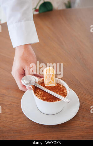 Garçon part de cuisine italienne Tiramisu en tasse blanche avec biscuit Savoiardi ladyfinger ou Banque D'Images