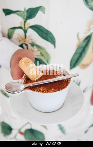 Garçon part de cuisine italienne Tiramisu en tasse blanche avec biscuit Savoiardi ladyfinger ou Banque D'Images