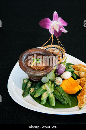 Pâte de crevettes épicées thaï chili plongeon dans la coupe du mortier avec un assortiment de légumes et œuf frit sur tableau noir Banque D'Images