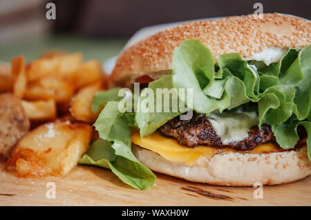 Cheeseburger bœuf, morceaux de pommes de terre frites avec sauce trempette ranch sur plaque en bois close up shot Banque D'Images