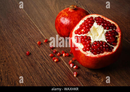 Stil life - toute rouge et coupé les fruits et graines de grenade éparpillés sur une table en bois foncé Banque D'Images