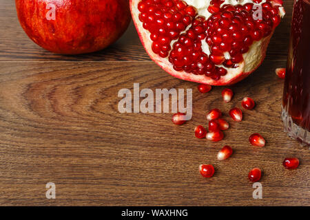 Stil life - toute rouge et coupé les fruits, graines de grenade dispersés et verre de jus de fruits sur une table en bois foncé Banque D'Images