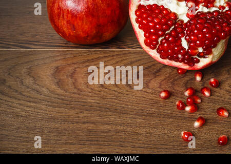 Stil life - toute rouge et coupé les fruits et graines de grenade éparpillés sur une table en bois foncé Banque D'Images