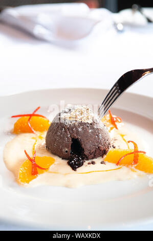 Dessert français. Fondant au chocolat Gâteau de lave avec de la sauce à la vanille, d'agrumes et de feuille d'or sur plaque blanche et la fourche Vue de côté Banque D'Images