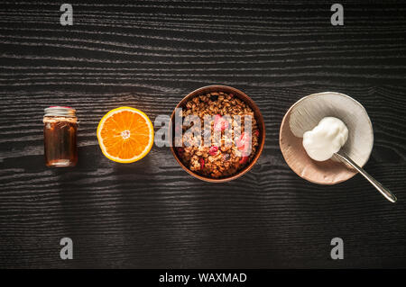 Petit déjeuner sain. muesli muesli aux fruits, yaourt et miel dans bol en bois sur fond noir Top view with copy space Banque D'Images