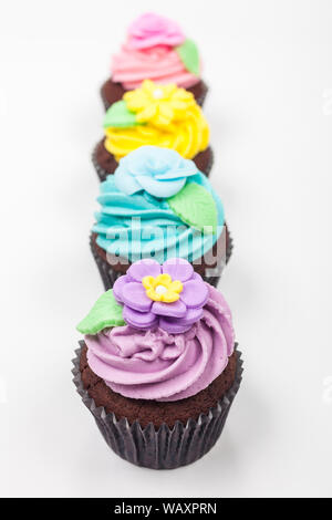 Quatre gâteaux de tasse de chocolat avec du glaçage ou de givre, rose, violet, bleu et jaune avec des feuilles vertes, photographié sur un fond blanc Banque D'Images