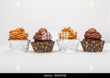 Quatre gâteaux de tasse avec du glaçage ou de givre, deux et deux au chocolat Caramel, photographié sur un fond blanc Banque D'Images