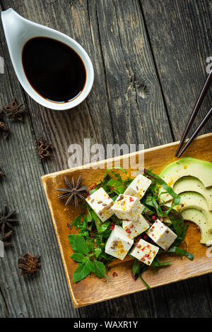 Le tofu dans une assiette et table en bois avec des légumes et fruits colorés avec de la sauce soja Banque D'Images