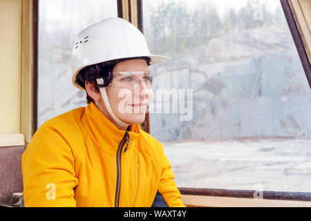 Femme dans un casque et des lunettes de protection dans la cabine de matériel de construction lourde Banque D'Images