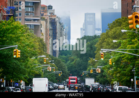 Les immeubles de Manhattan skyline à partir de la 5e avenue à Harlem un jour brumeux, à travers les arbres et les feux de circulation. New York, USA. Banque D'Images