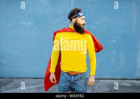 Portrait d'un homme comme un super héros dans des vêtements colorés et lunettes de pilote sur le fond bleu Banque D'Images