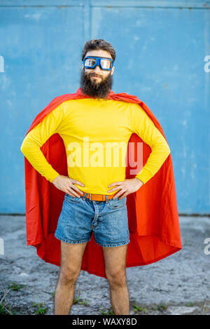 Portrait d'un homme comme un super héros dans des vêtements colorés et lunettes de pilote sur le fond bleu Banque D'Images