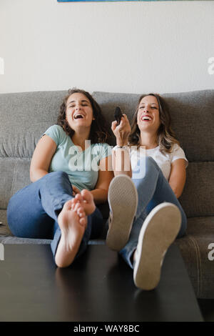 Les filles dans une table avec pieds d'une table regardant la télévision heureusement Banque D'Images