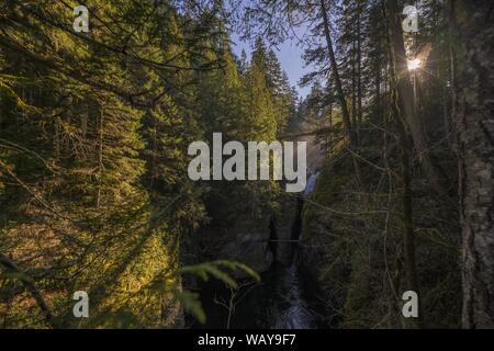 Le lac coule entre les falaises entourées d'arbres avec le soleil rayons pénétrant à travers leurs branches Banque D'Images