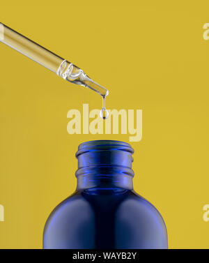 Huiles Essentielles flacon avec compte-gouttes et une goutte suspendue sur fond jaune Banque D'Images