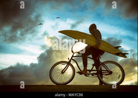 Silhouette de surfer carrying his surfboard sur une plage en vtt en face de ciel lumineux Banque D'Images