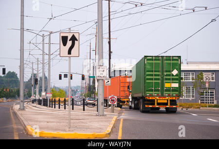 Convoi de puissantes plates-formes professionnelles grand semi camions transportant des conteneurs industriels avec la cargaison commerciale fonctionnant sur la rue de la ville avec tram lin Banque D'Images