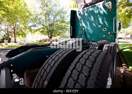 Les roues arrière de la bande de roulement des pneus d'un gros camion professionnel puissant vert semi truck tracteur garé sur une rue sous les arbres verts Banque D'Images