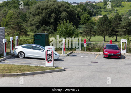 Tesla Supercharger Gare vu tandis qu'un modèle Tesla blanc et rouge 3 une Tesla Model S sont garées et de charge. Banque D'Images