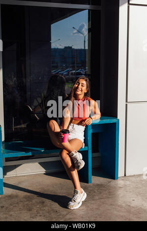 Heureux élégant jeune brunette woman wearing white shorts et baskets rose holding tasse de café d'aller. Banque D'Images