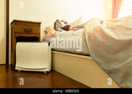 Purificateur d'air dans la chambre à coucher avec jeune garçon qui s'étend sur le lit. Banque D'Images