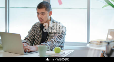 Les jeunes créateurs qui travaillent dur à travailler sur son projet tout en tapant sur l'ordinateur portable en chambre confortable Banque D'Images