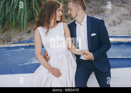 Belle jeune femme aux cheveux longs en robe blanche avec son jeune mari sur la plage Banque D'Images