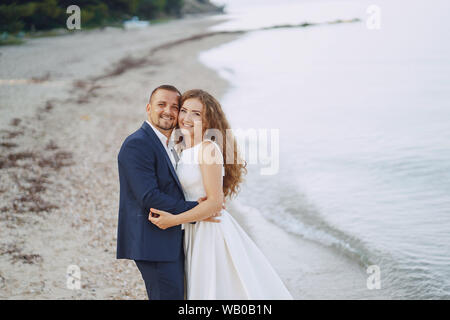 Belle jeune femme aux cheveux longs en robe blanche avec son jeune mari sur la plage Banque D'Images