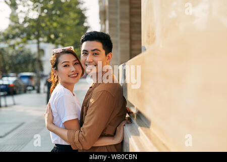 Vue arrière d'un jeune couple hugging dans une ville de destination tout en se tenant dans le quartier commerçant à proximité d'un magasin de chaussures de qualité de luxe, à l'extérieur Banque D'Images