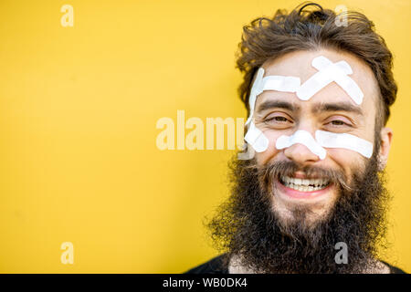 Close-up portrait d'un homme blessé avec des patchs sur son visage sur le baackground jaune Banque D'Images