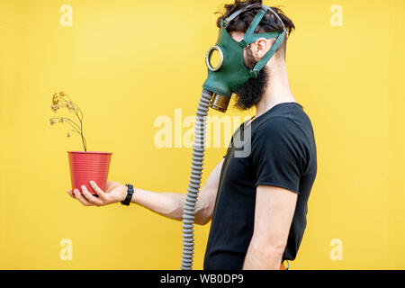 Portrait d'un homme triste avec masque à gaz et séché sur le pot de fond jaune. Concept de l'écologie, la pollution de l'air pauvre et des dangers d'irradiation Banque D'Images