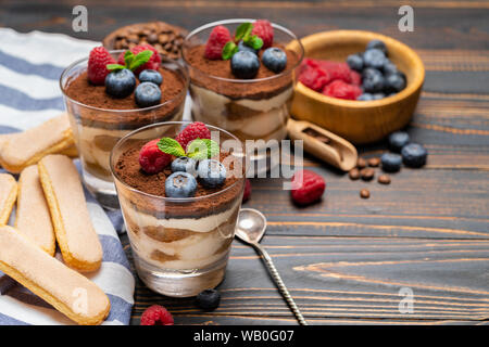 Dessert tiramisu classique avec les bleuets et les fraises dans une coupe en verre et les biscuits savoiardi sur fond de bois Banque D'Images