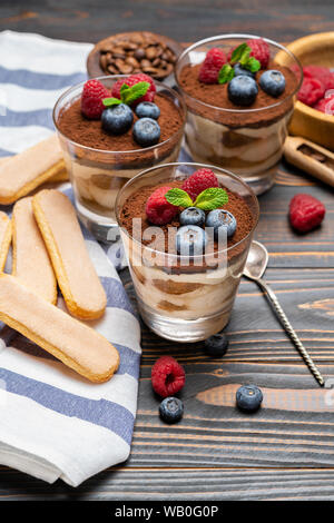 Dessert tiramisu classique avec les bleuets et les fraises dans une coupe en verre et les biscuits savoiardi sur fond de bois Banque D'Images